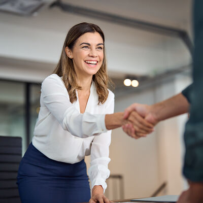 Happy mid aged business woman manager handshaking greeting client in office.